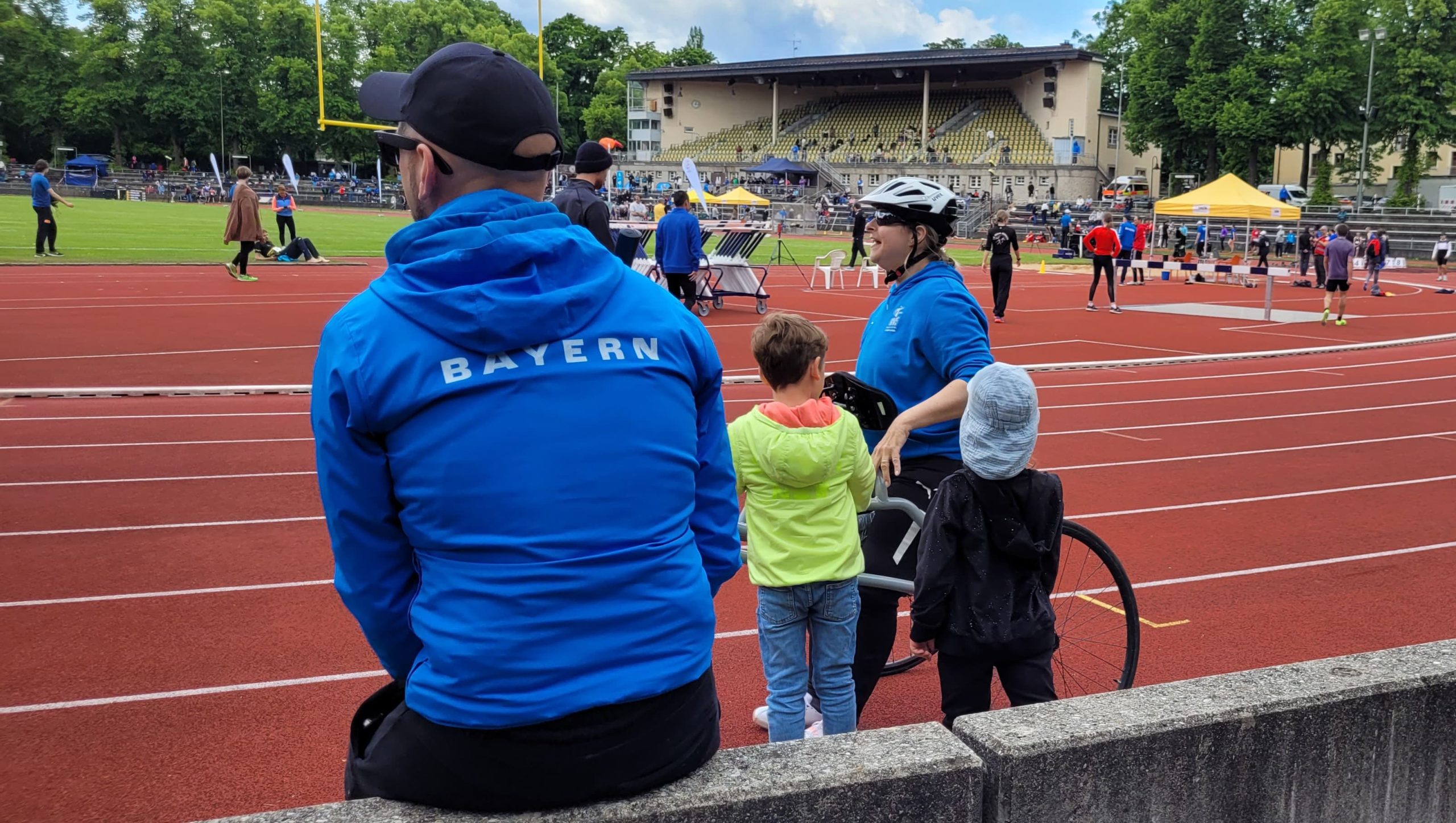 Stefan von hinten mit seinem Bayern-Hoodie wartet am Spielfeldrand sitzend auf einer kleinen Mauer.